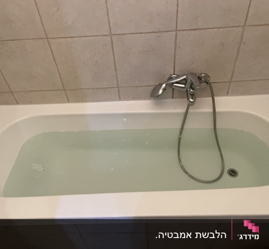 אמבטיה עם מים וברז מתכת על קיר מרוצף